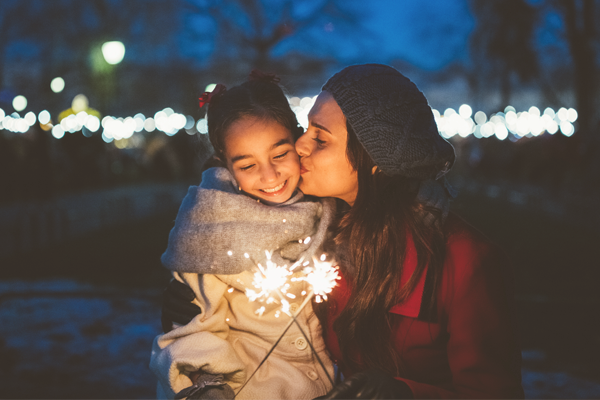 Woman and her daughter hold sparklers on a winter night